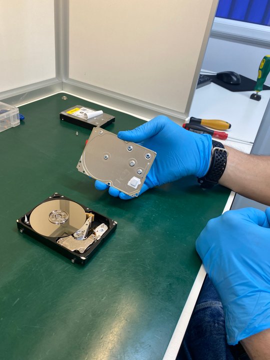 Gloved engineer holding 2.5-inch HDD above opened drive for donor matching