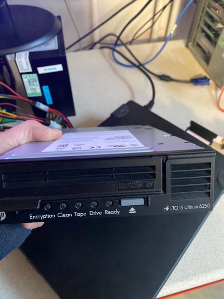 Engineer holding HP LTO-6 Ultrium tape drive in lab with equipment in background