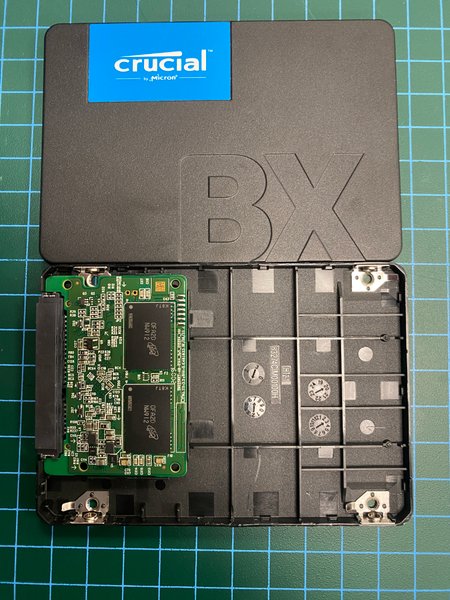 Opened Crucial BX SSD showing NAND PCB inside plastic shell on green grid mat